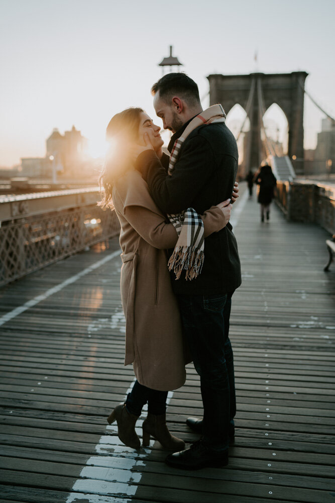 Couple snuggling on brooklyn bridge at sunrise during engagement session