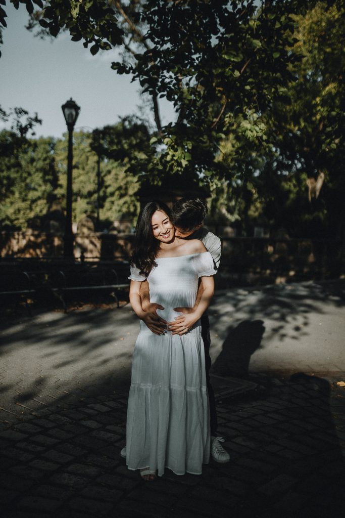 Expecting couple snuggling in central park during maternity photoshoot