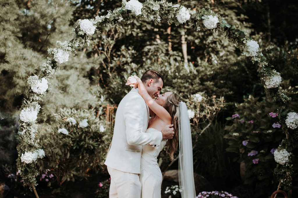 Bride and groom kiss under arch at hamptons backyard wedding