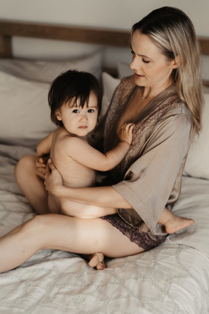 Baby girl snuggling on bed with mom during breastfeeding photoshoot