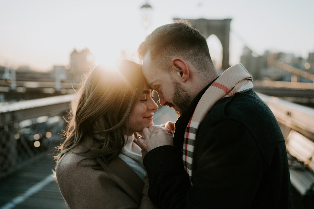 Couple snuggling on brooklyn bridge at sunrise during engagement session