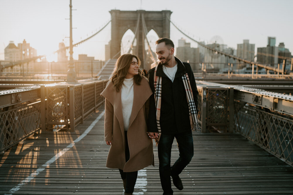 Couple walking on brooklyn bridge at sunrise during engagement session