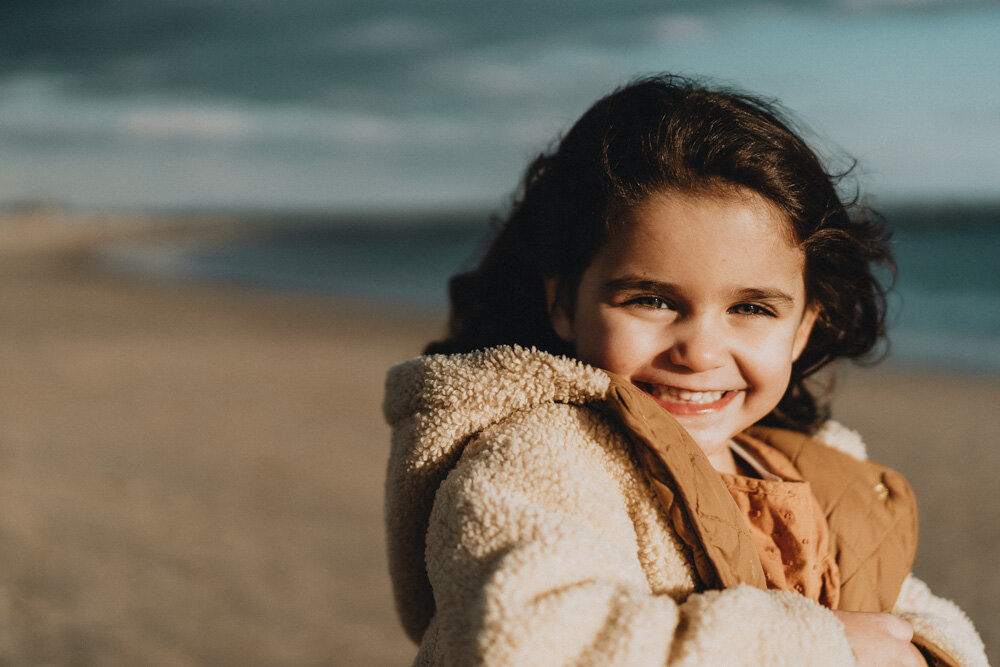 Young girl smiles at photographer during family session at coney island beach