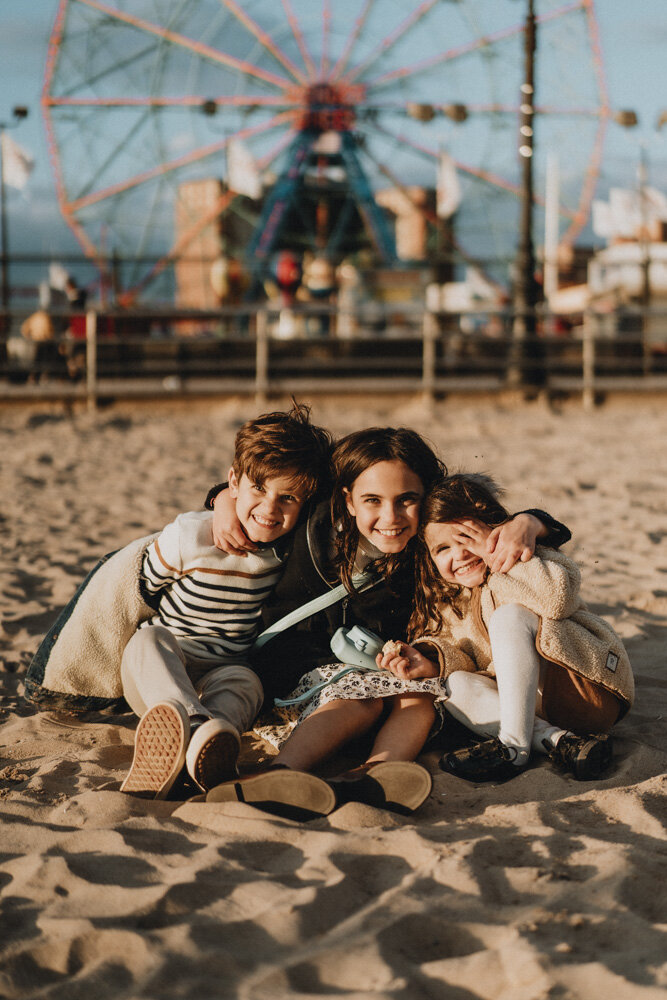 Three kids smile at photographer during family session at coney island beach
