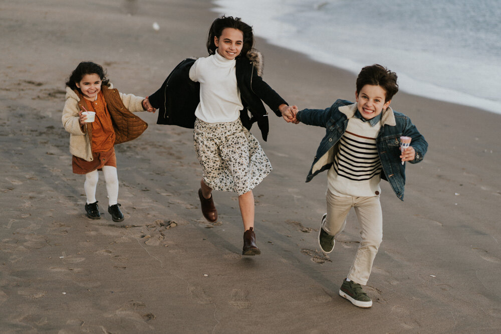 Three kids hold hands during family session at coney island beach