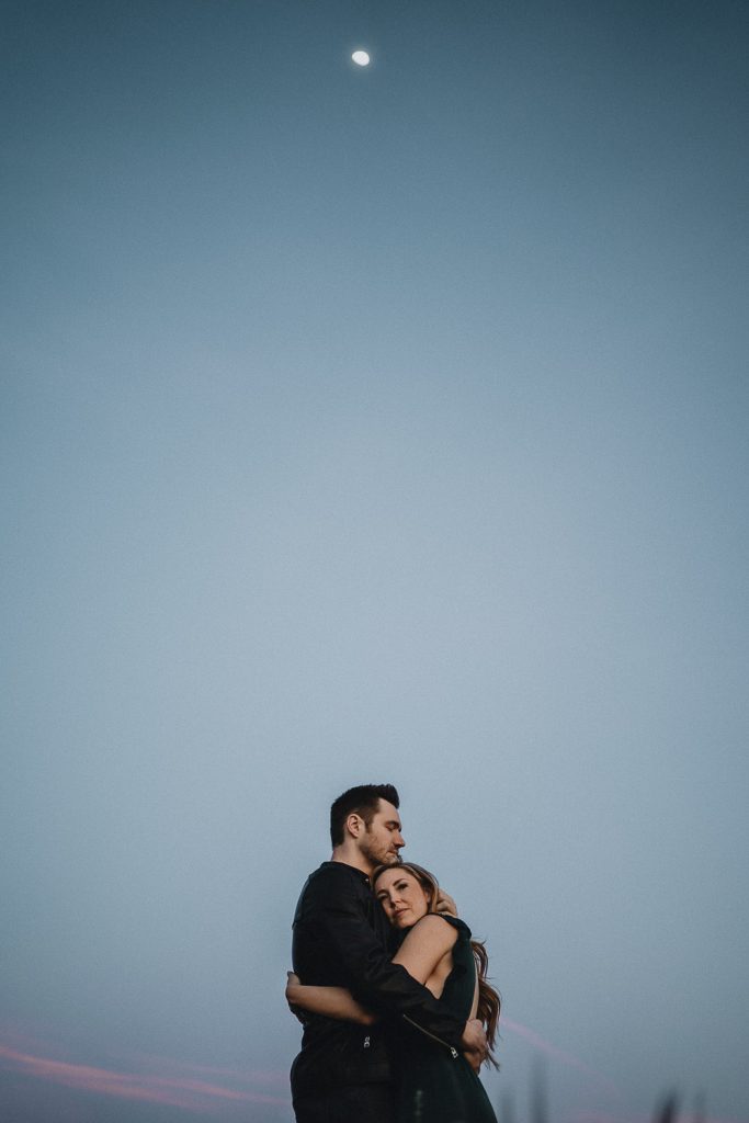 Couple hugging at blue hour with moon up in the sky