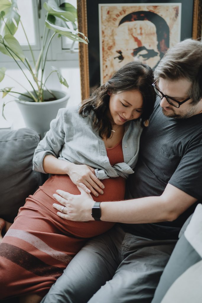 Expecting couple touches baby bump during in home maternity session in brooklyn