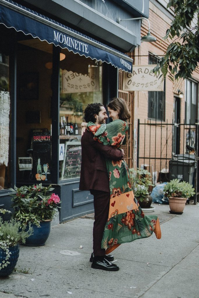 Groom carries bride in front of brooklyn restaurant during elopement