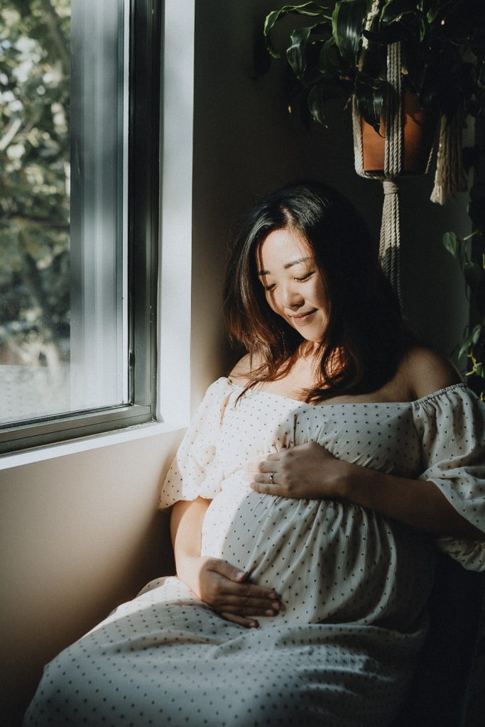 Pregnant woman in patch of light by window during maternity session
