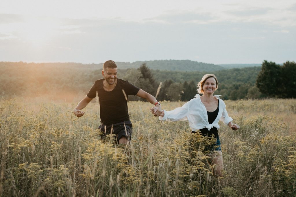 Couple running in field during golden hour engagement session upstate ny